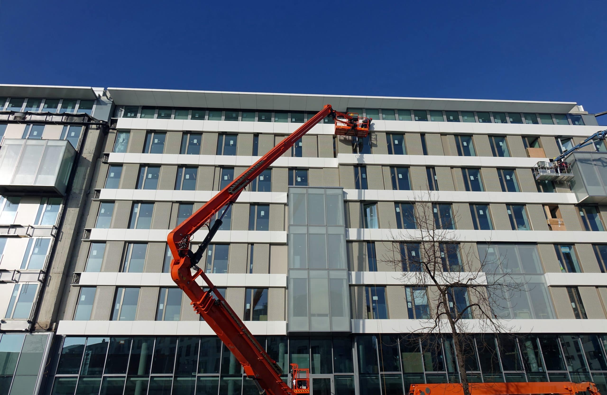 Nacelles sur un chantier de construction Ouvrier dans une grande nacelle travaillant sur la façade d'un bâtiment pendant une formation R486